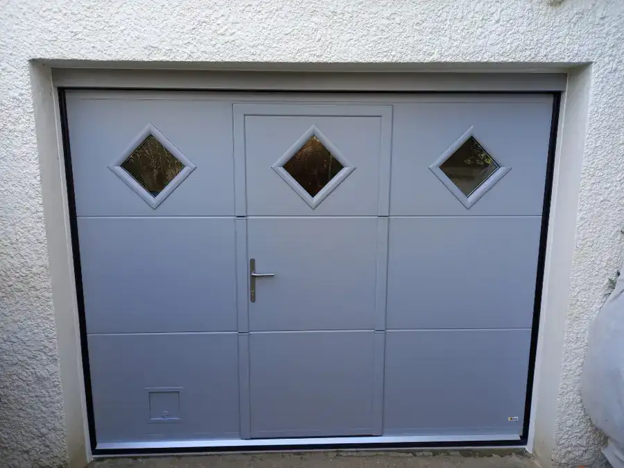 Porte de garage sectionnelle grise avec portillon et hublots losange